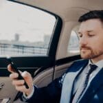 A businessman in a luxury car, reviewing information on his smartphone during transit.