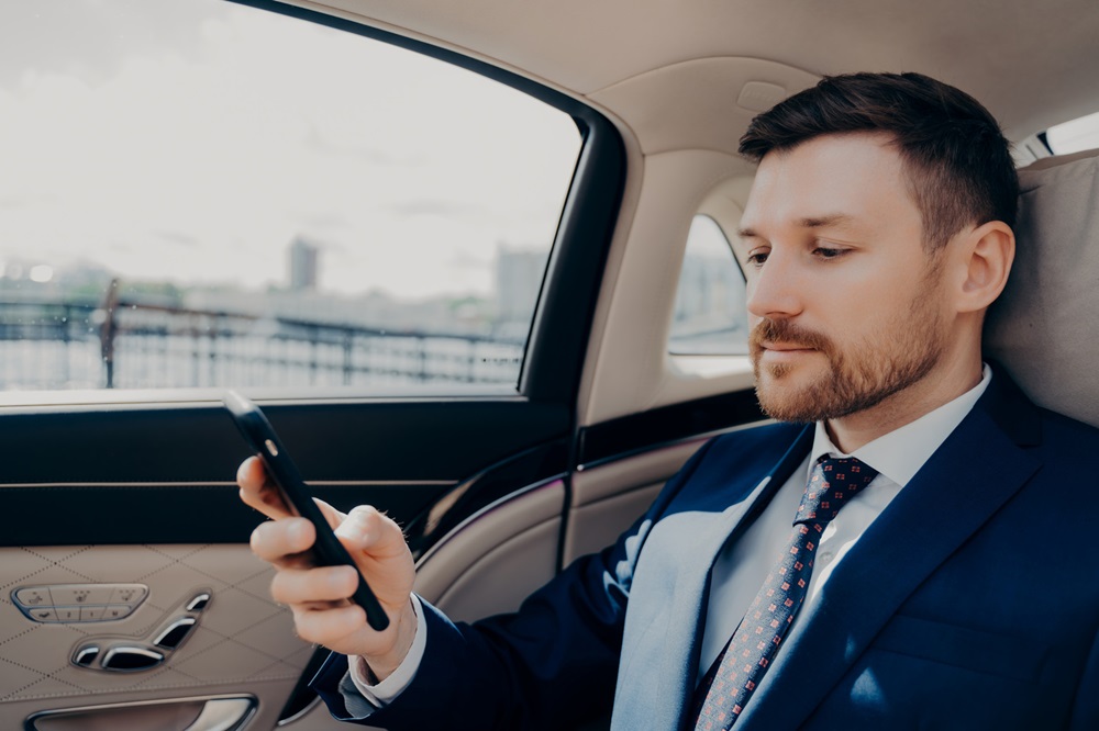 A businessman in a luxury car, reviewing information on his smartphone during transit.