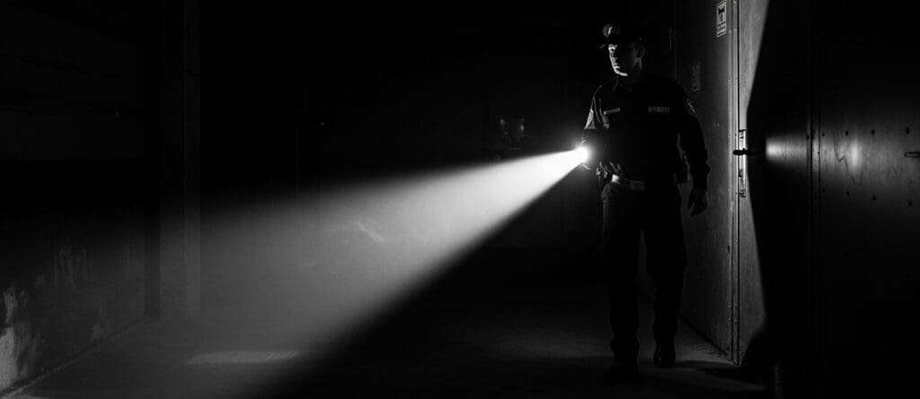 A patrolling security guard in the dark with a flashlight.